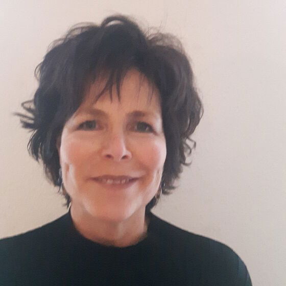 Eine Frau mit dunklen, kurzen Haaren und schwarzem Shirt steht vor hellem Hintergrund.