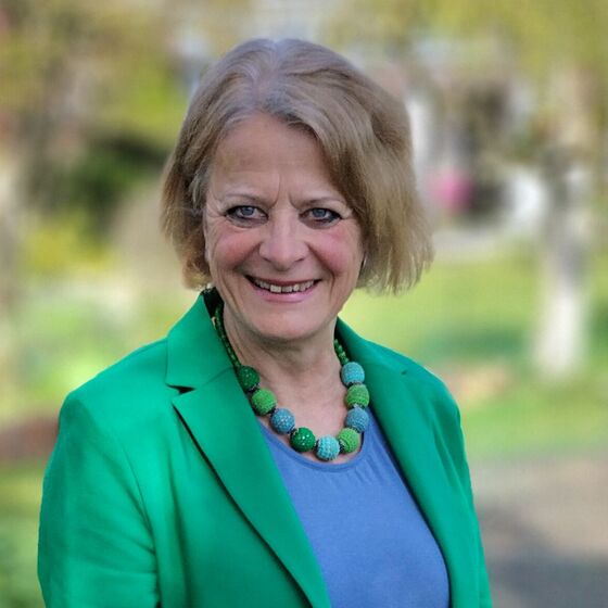 Eine blonde, ergrauende ältere Frau lächelt in die Kamera. Sie trägt einen grünen Blazer über einem blauen Shirt.