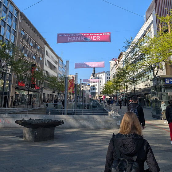 Banner mit Kirchentagsschriftzug hängt über einer Einkaufsstraße in Hannovers Innenstadt.