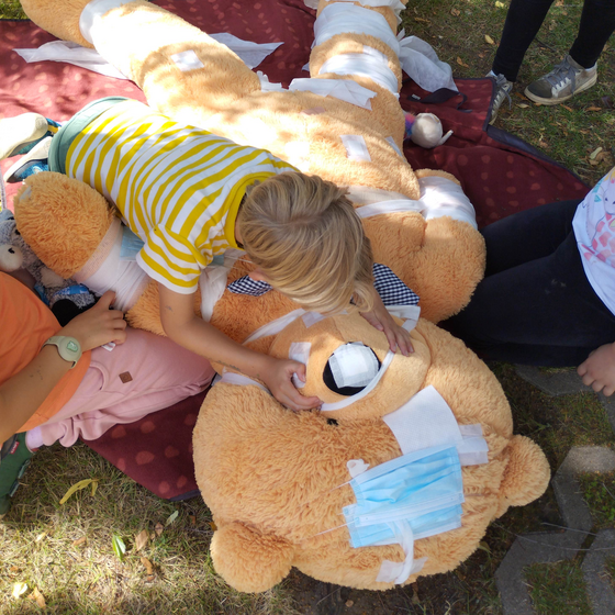 Ein Kind beugt sich über einen Riesen-Teddy, der mehrere Verbände und Masken trägt.