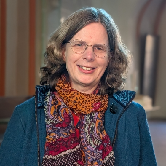 Eine weiblich gelesene Person mit mittellangen Haaren und buntem Schal in einer Kirche.