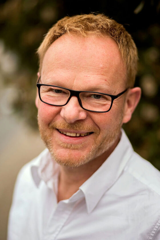 Ein Mann mit kurzen Haaren, Vollbart und Brille blickt in die Kamera.