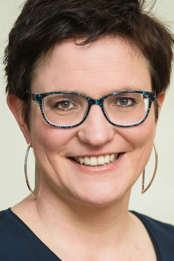 Eine als Frau lesbare Person mit kurzen dunklen Haaren und Brille
