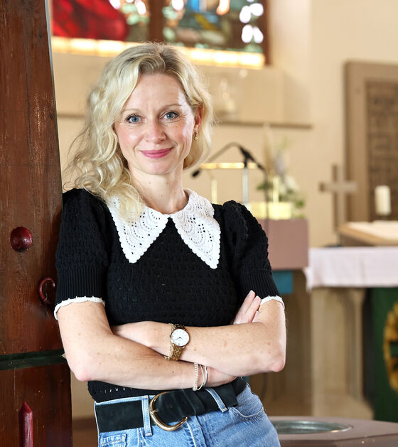 Eine als Frau lesbare Person lehnt in einer Kirche an einer Holzsäule.