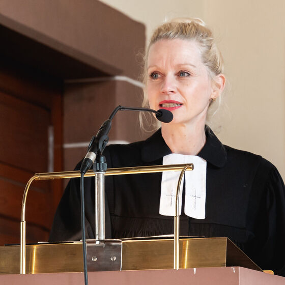 Eine als Frau lesbare Person im Talar predigt an einem Lesepult.