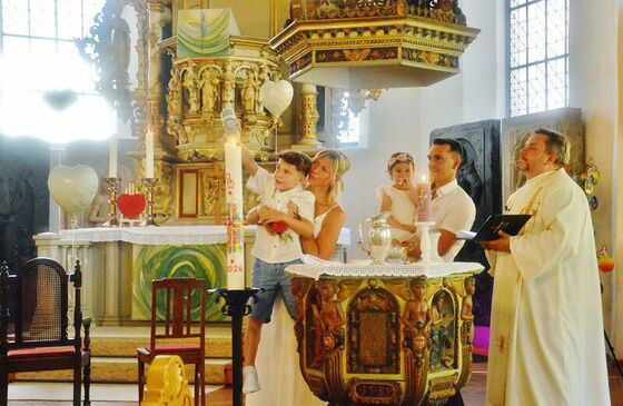 Eine Familie und ein Pastor stehen an einem Taufbecken in einer Kirche. Ein Junge zündet eine Taufkerze an.