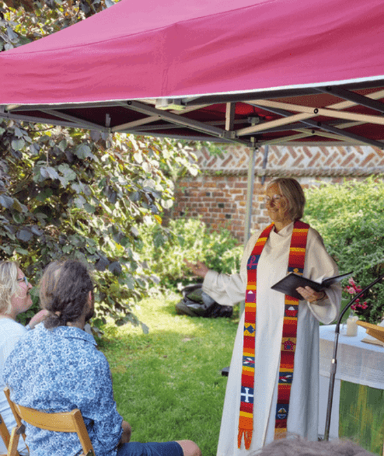 Eine Pastorin predigt unter einem Pavillon in einem Garten.