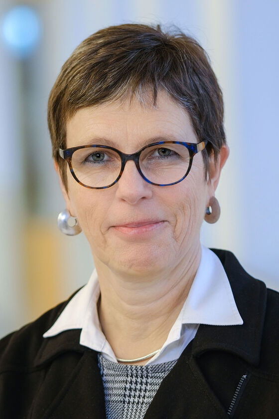 Eine weiblich gelesene Person mit kurzen dunklen Haaren und einer Brille mit dunkler Fassung. 