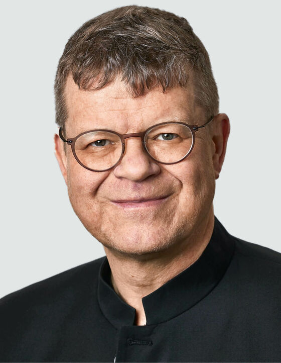 Eine als Mann lesbare Person mit Brille schaut in die Kamera.