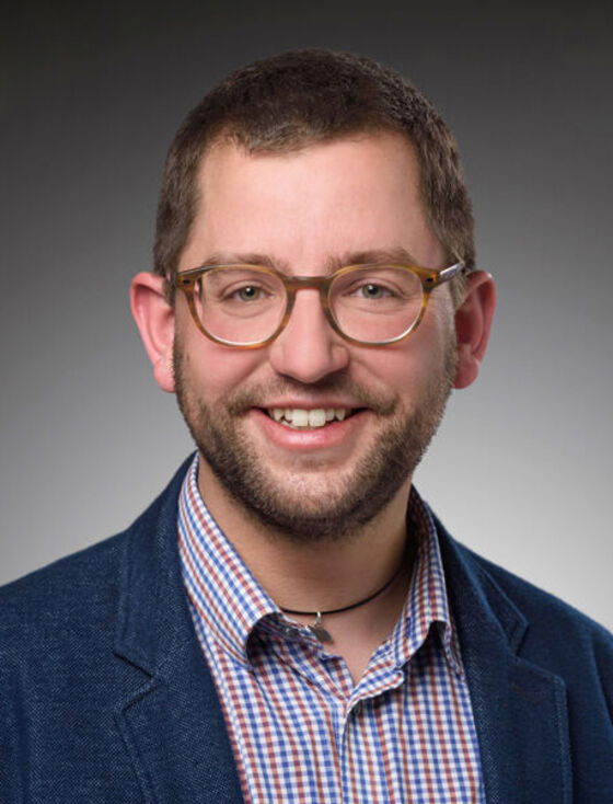 Eine als Mann lesbare Person mit kurzen Haaren und Brille.