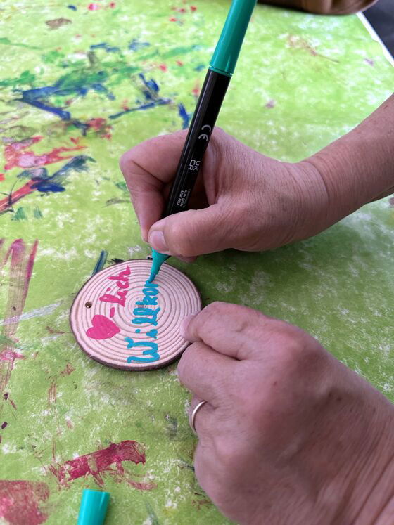 Jemand schreibt mit einem Stift "Herzlich Willkommen" auf eine kleine Baumscheibe.