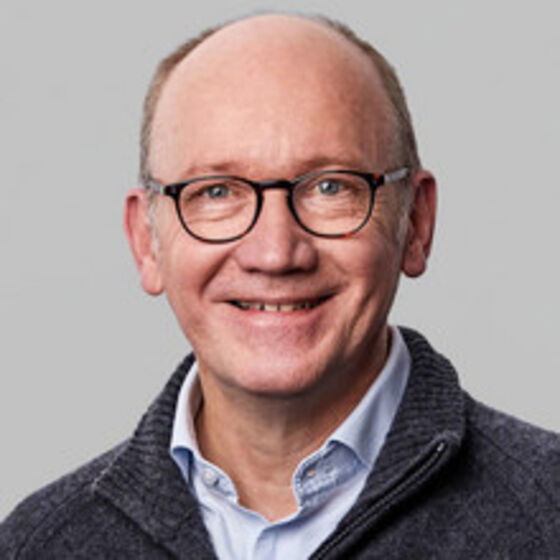 Eine als Mann lesbare Person mit hoher Stirn und Brille.