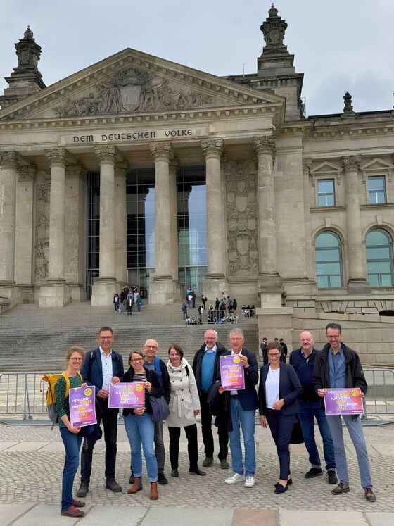 Eine Gruppe aus als Männern und Frauen lesbare Personen vor dem Berliner Reichstag.