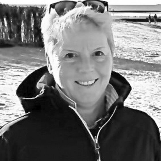 Eine als Frau lesbare Person mit hochgesteckter Sonnenbrille am Strand