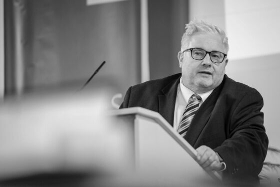 Eine männlich zu lesende Person steht an einem Redepult