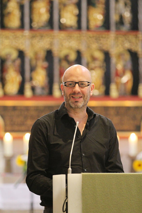 Eine als Mann lesbare Person spricht an einem Redepult in einer Kirche