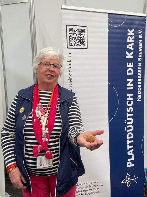 Eine als Frau lesbare ältere Person hält eine Walnuss in der Hand.