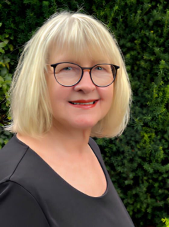 Auf dem Bild ist eine blonde Frau mit roter Brille zu sehen.