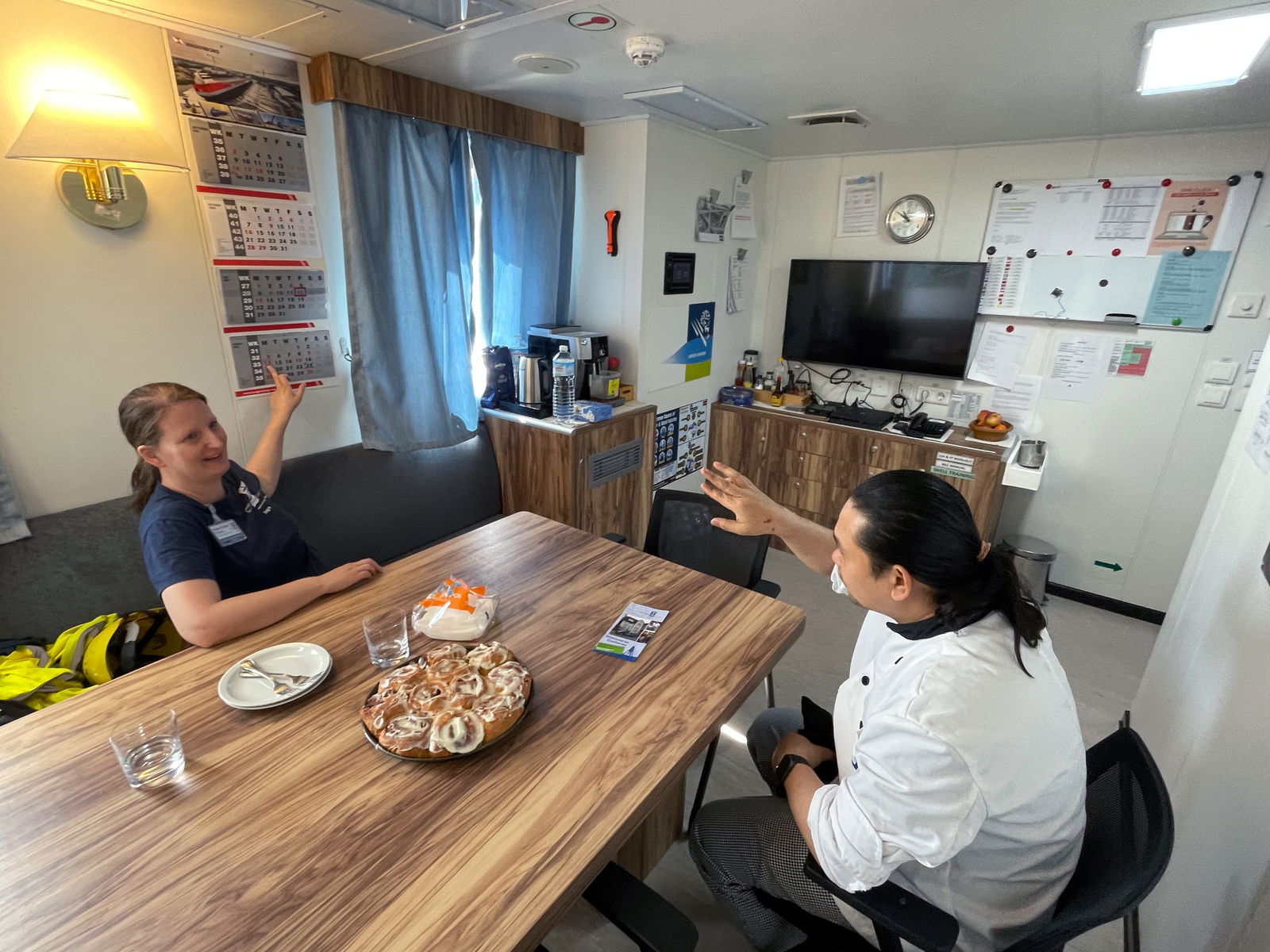 Zwei Personen sitzen um einen Tisch und reden und essen Zimtschnecken.