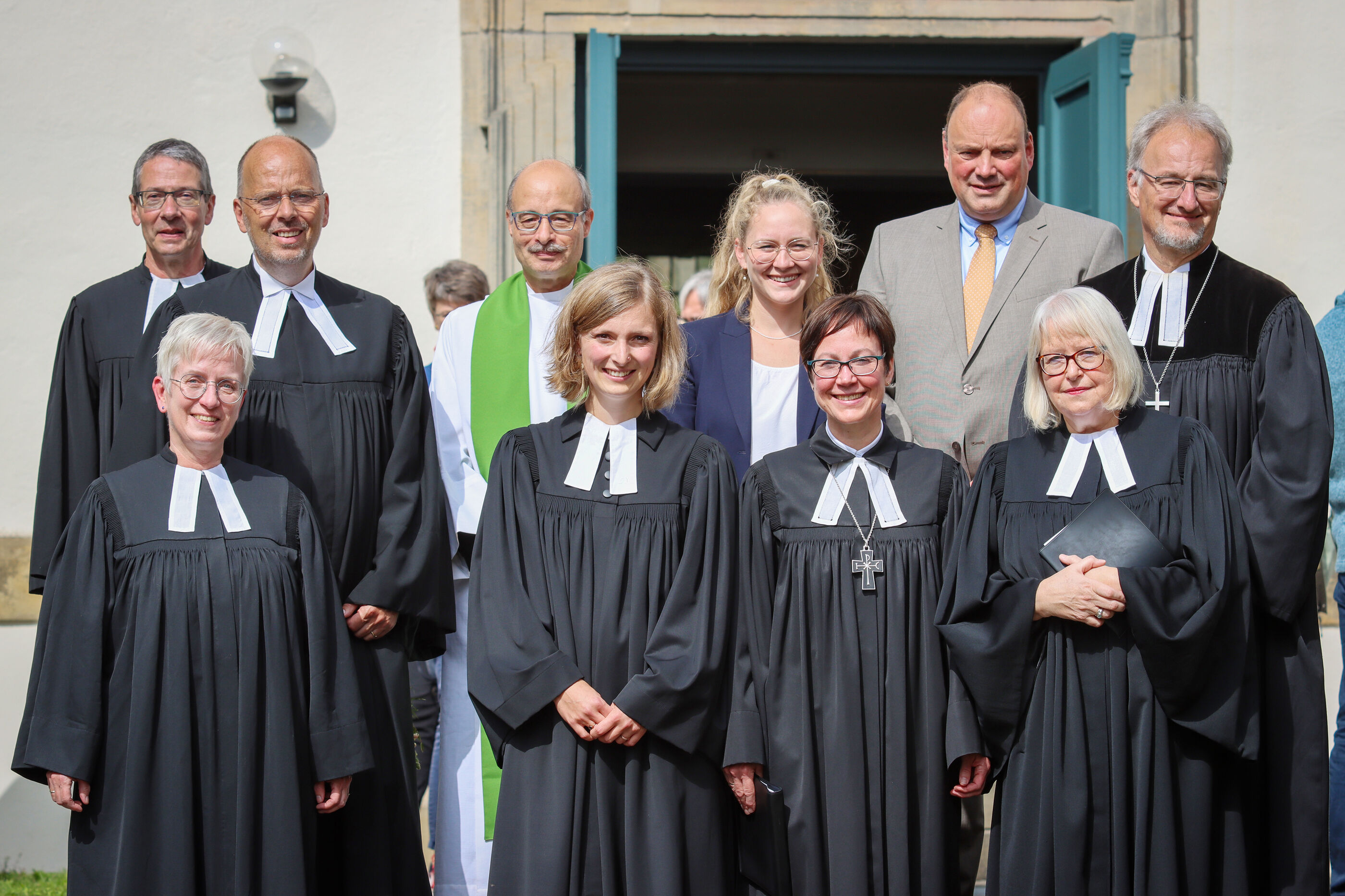 Pastorinnen und Pastoren stehen vor dem Eingang einer Kirche.