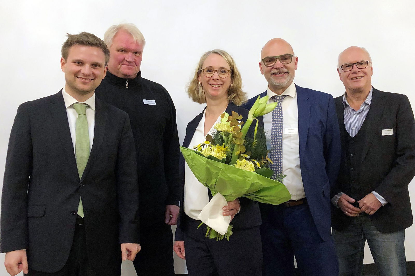 Gruppenbild mit vier Männern und einer Frau, die einen Blumenstrauß hält.