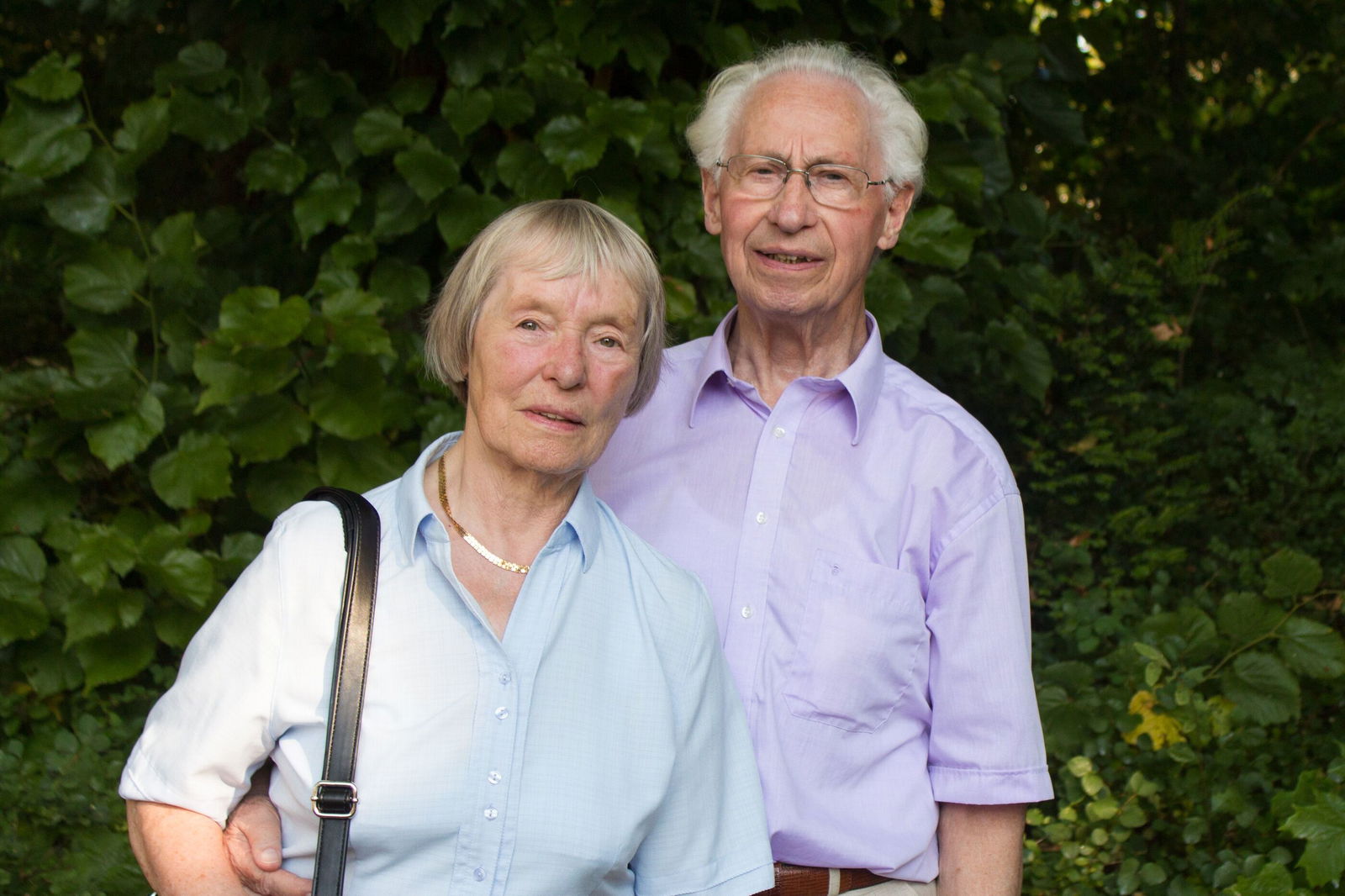 Ein älteres Paar vor grünen Büschen und Bäumen.