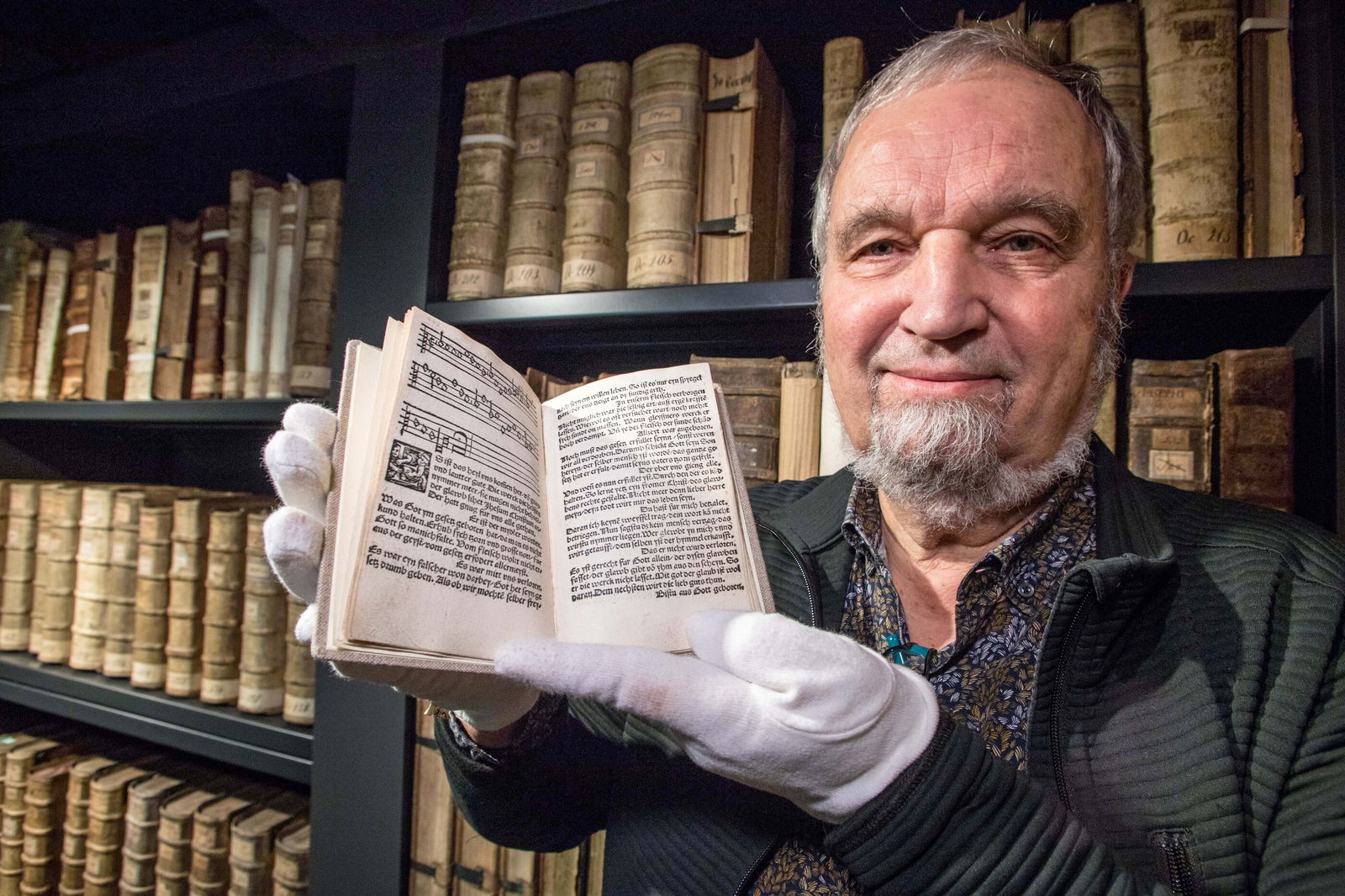 Ein Mann hält mit weißen Handschuhen ein sehr altes Gesangbuch.
