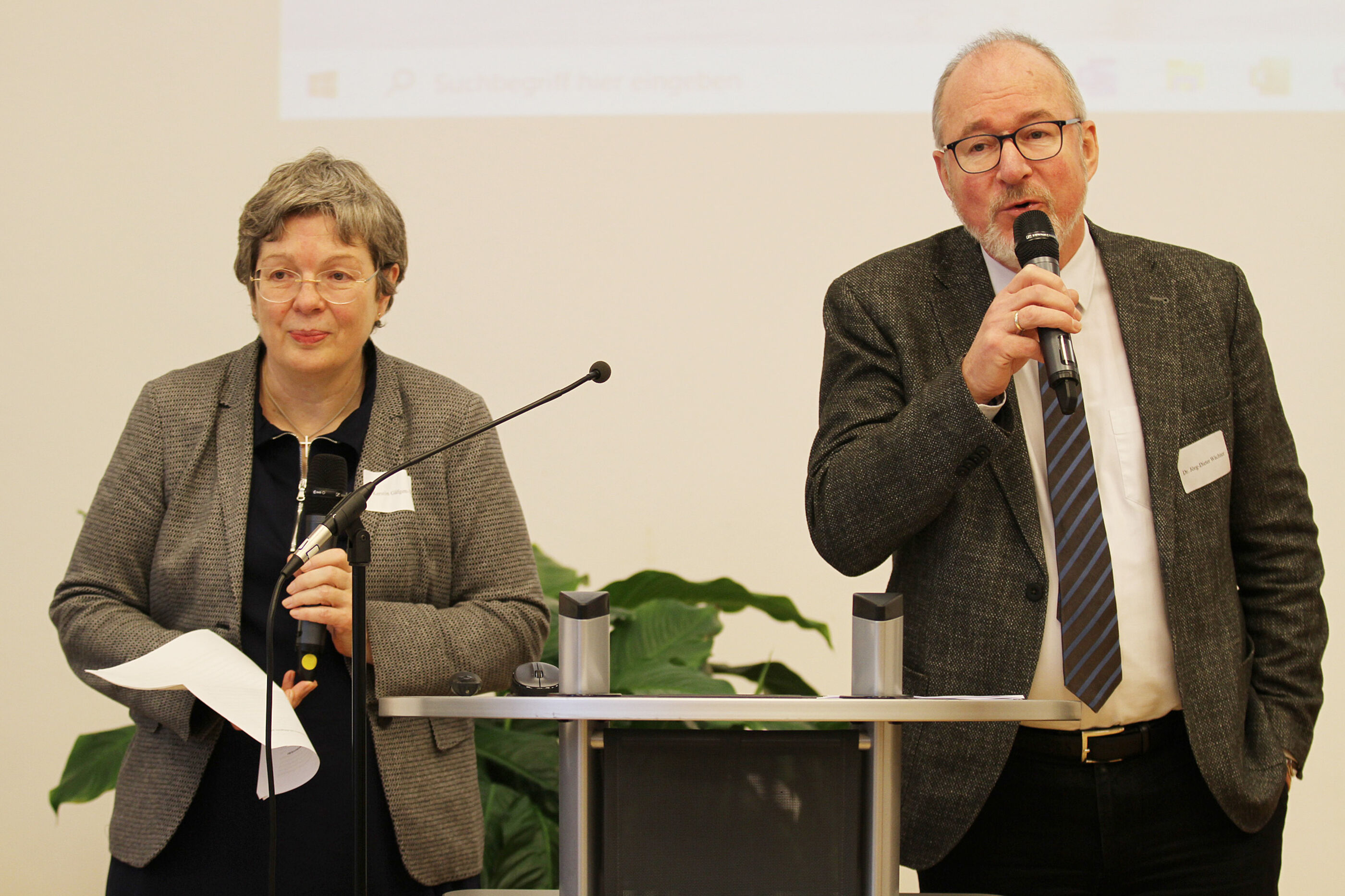 Eine ältere Frau und ein älterer Mann stehen an einem Pult und sprechen in ein Mikrofon.
