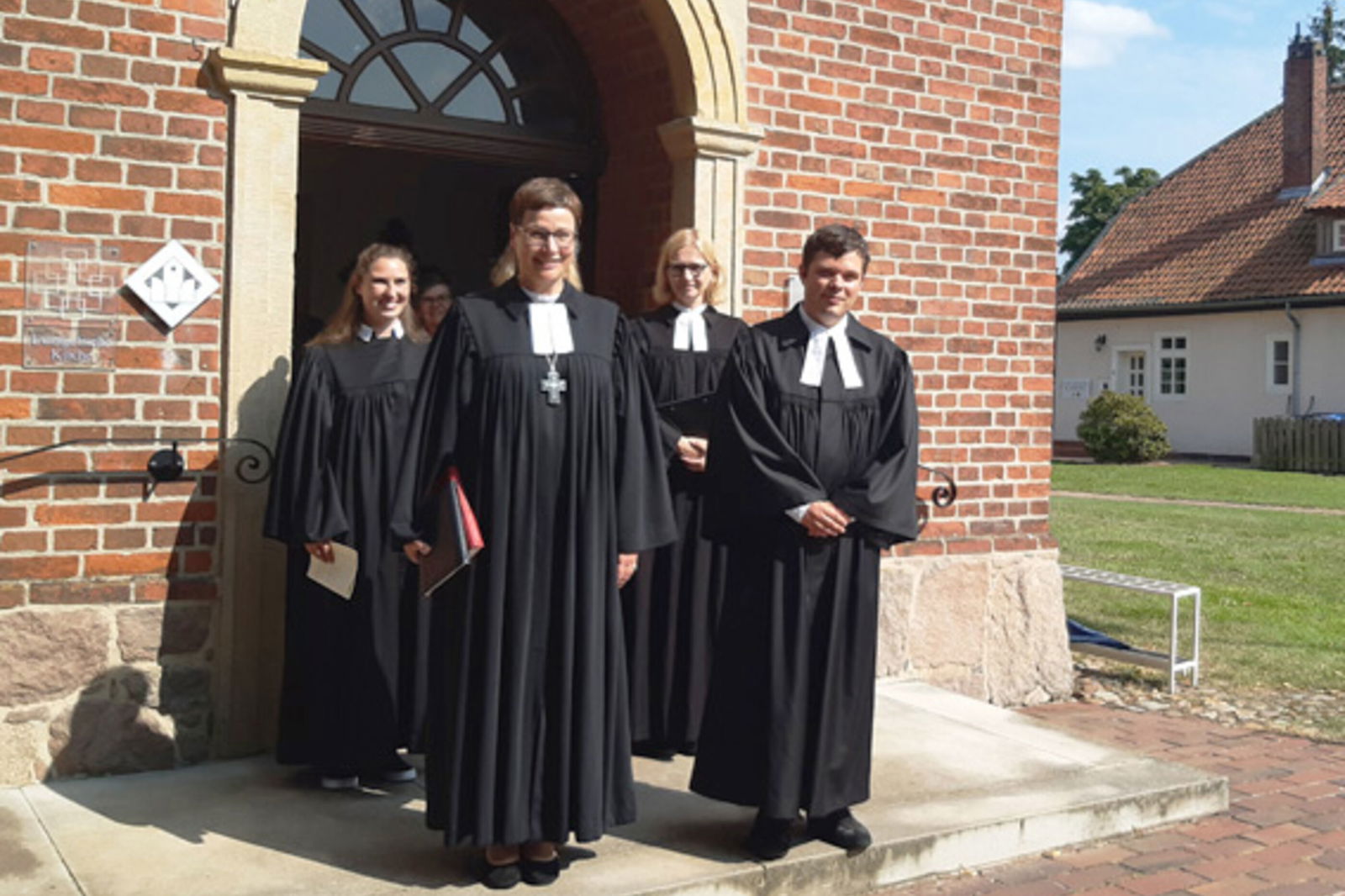 eine Gruppe von Menschen in schwarzen Talaren vor einer Kirche.