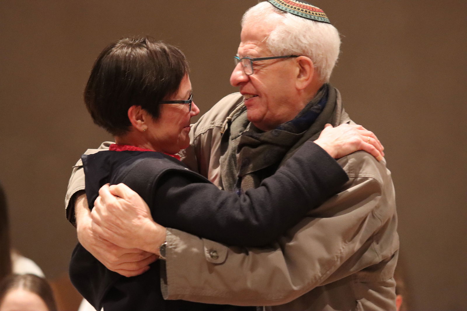 Eine weiblich und eine männlich gelesene Personen umarmen sich. Der rechte trägt eine Kippa.