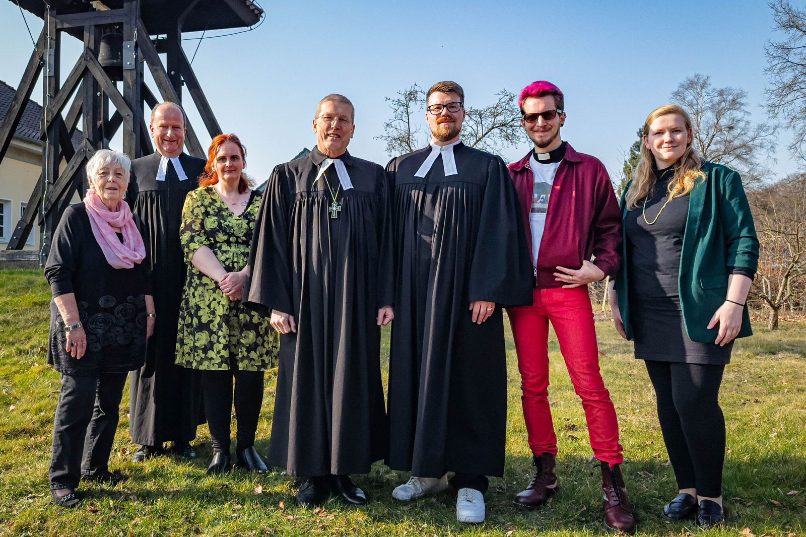 Sieben Personen, drei davon im Talar, stehen zusammen auf einer grünen Fläche.