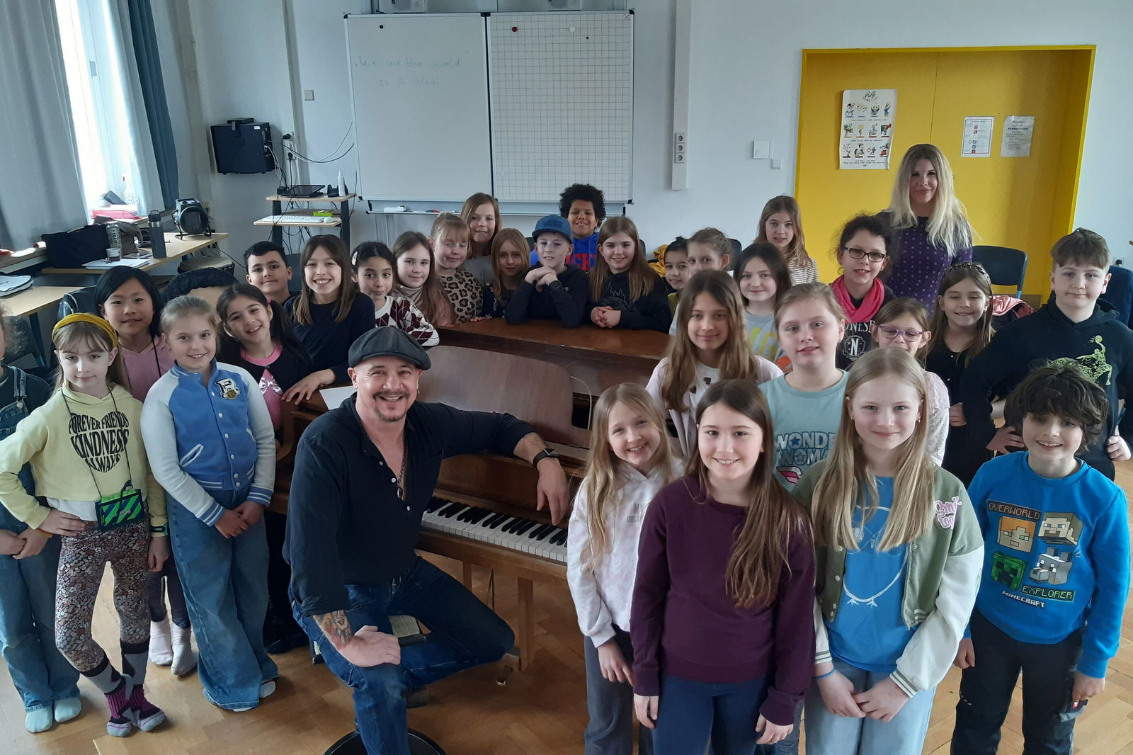 Eine Gruppe Kinder steht um ein Klavier, an dem eine erwachsene, männlich gelesene Person sitzt.