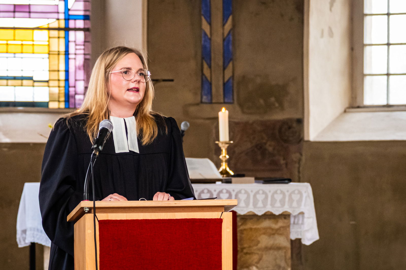 Eine junge, blonde, weiblich gelesene Person steht im Talar an einem Redepult.