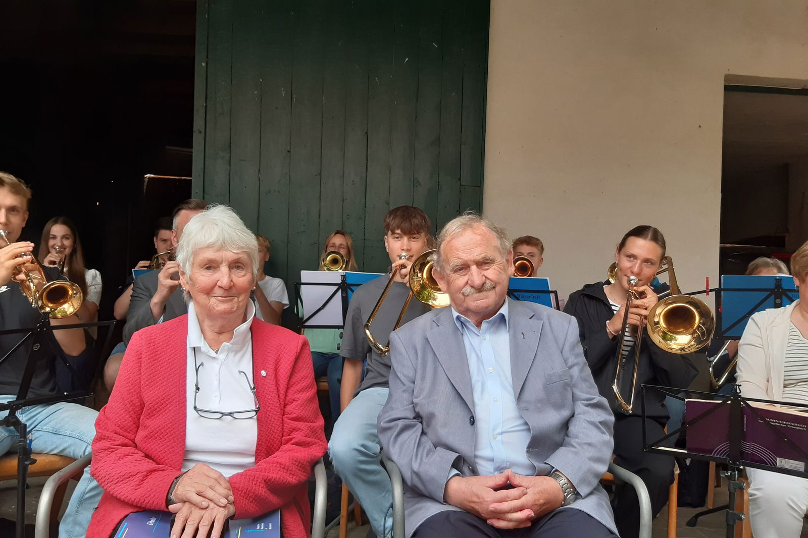 Eine Frau und ein Mann sitzen umringt von anderen Menschen, die applaudieren.