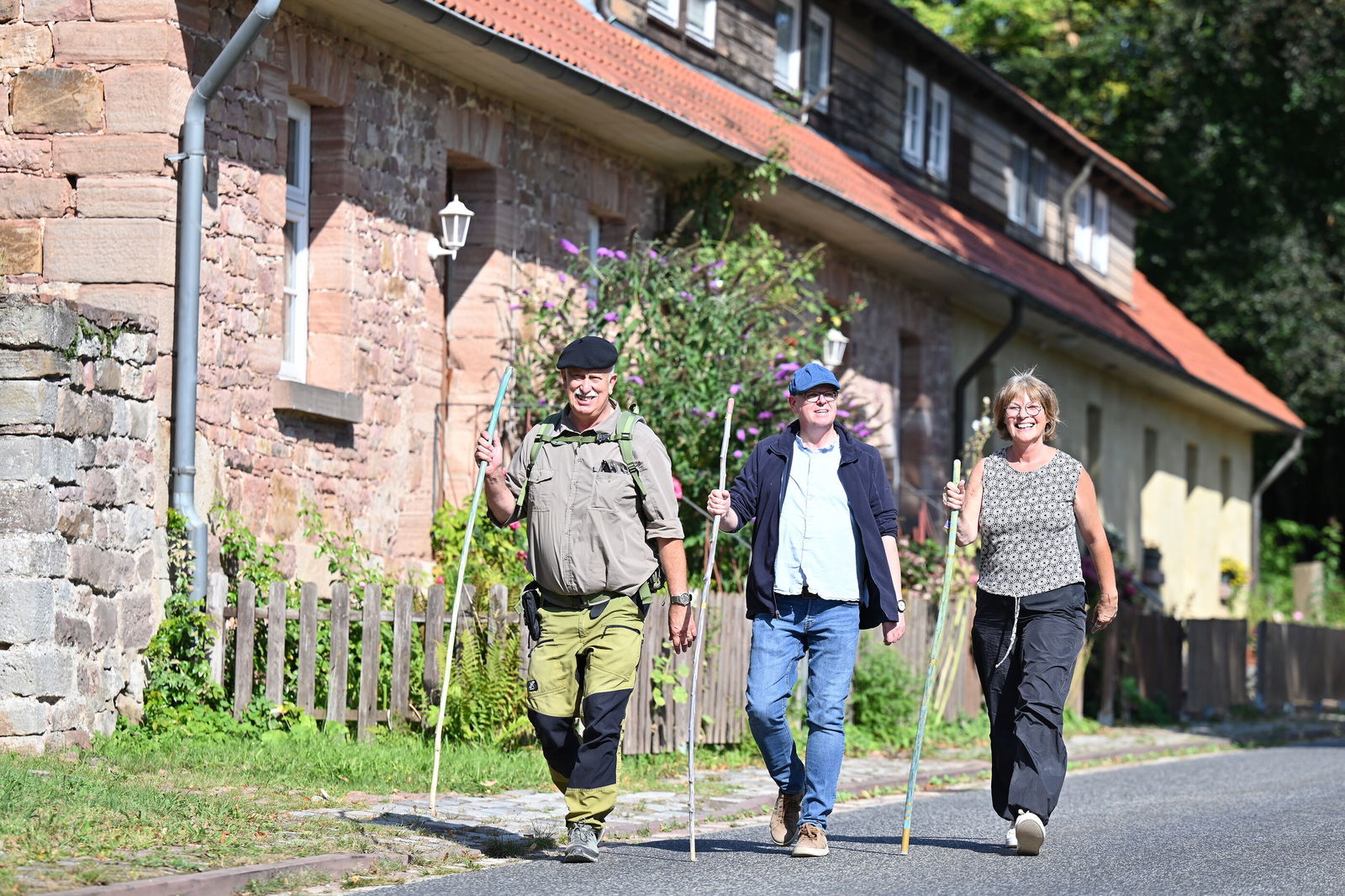 Drei Personen wandern vor einem historischen Gebäude.