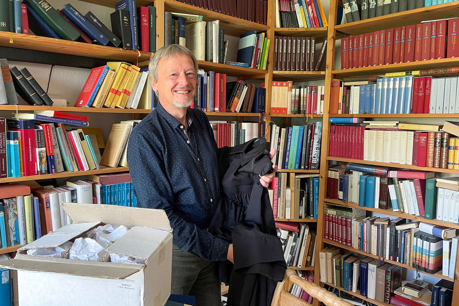 Ein Mann mit Kartons steht vor einem vollen Bücherregal.