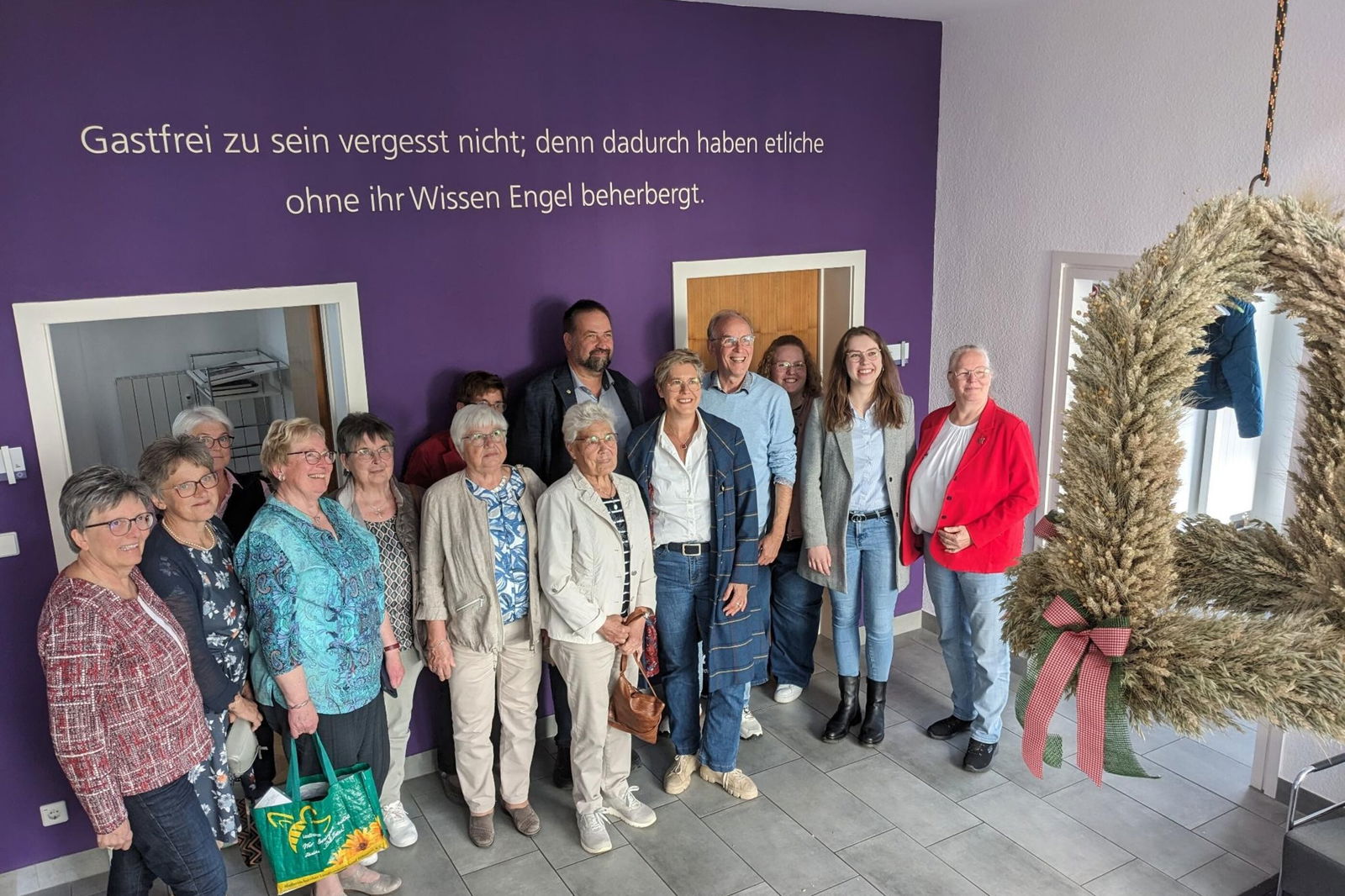 Mehrere Personen stehen  vor einer lila Wand und schauen auf eine Erntekrone.