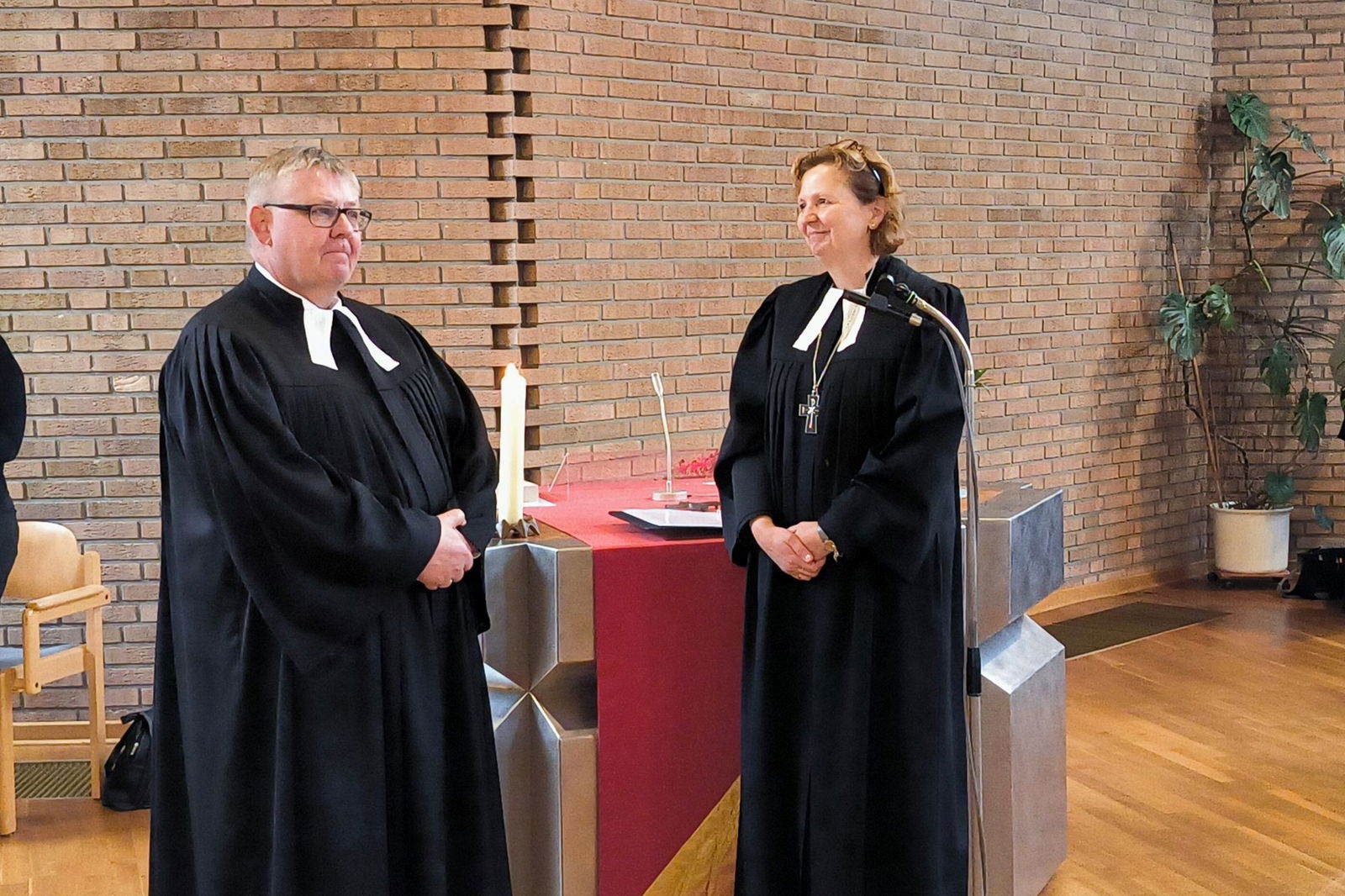 Zwei Menschen, ein Mann und eine Frau, im Talar vor einem Altar-