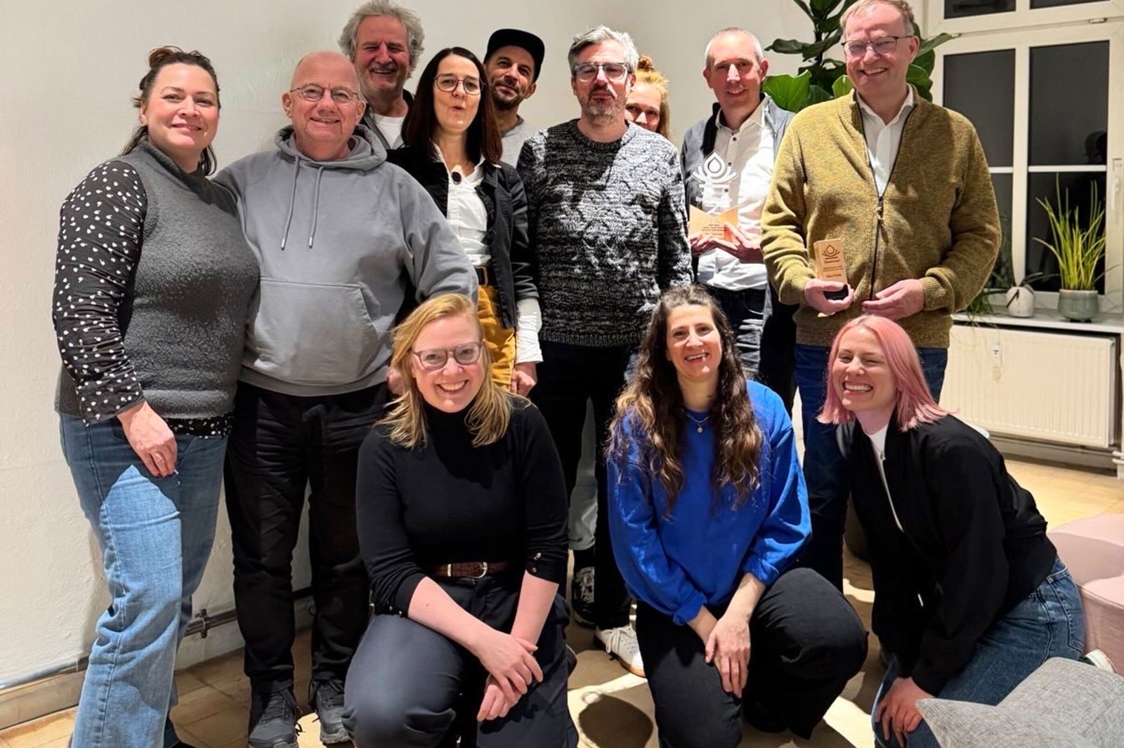 Eine Gruppe aus als Männer und Frauen lesbare Personen posieren in einem Raum für ein Gruppenfoto.
