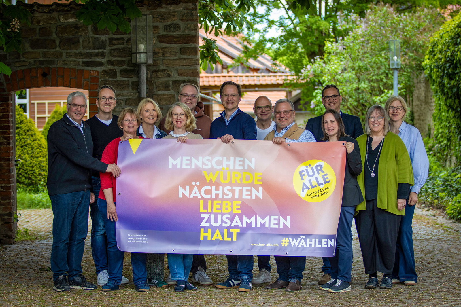 Eine Gruppe aus als Männer und Frauen lesbare Personen hält ein Transparent mit der Aufschrift Menschenwürde, Nächstenliebe, Zusammenhalt.