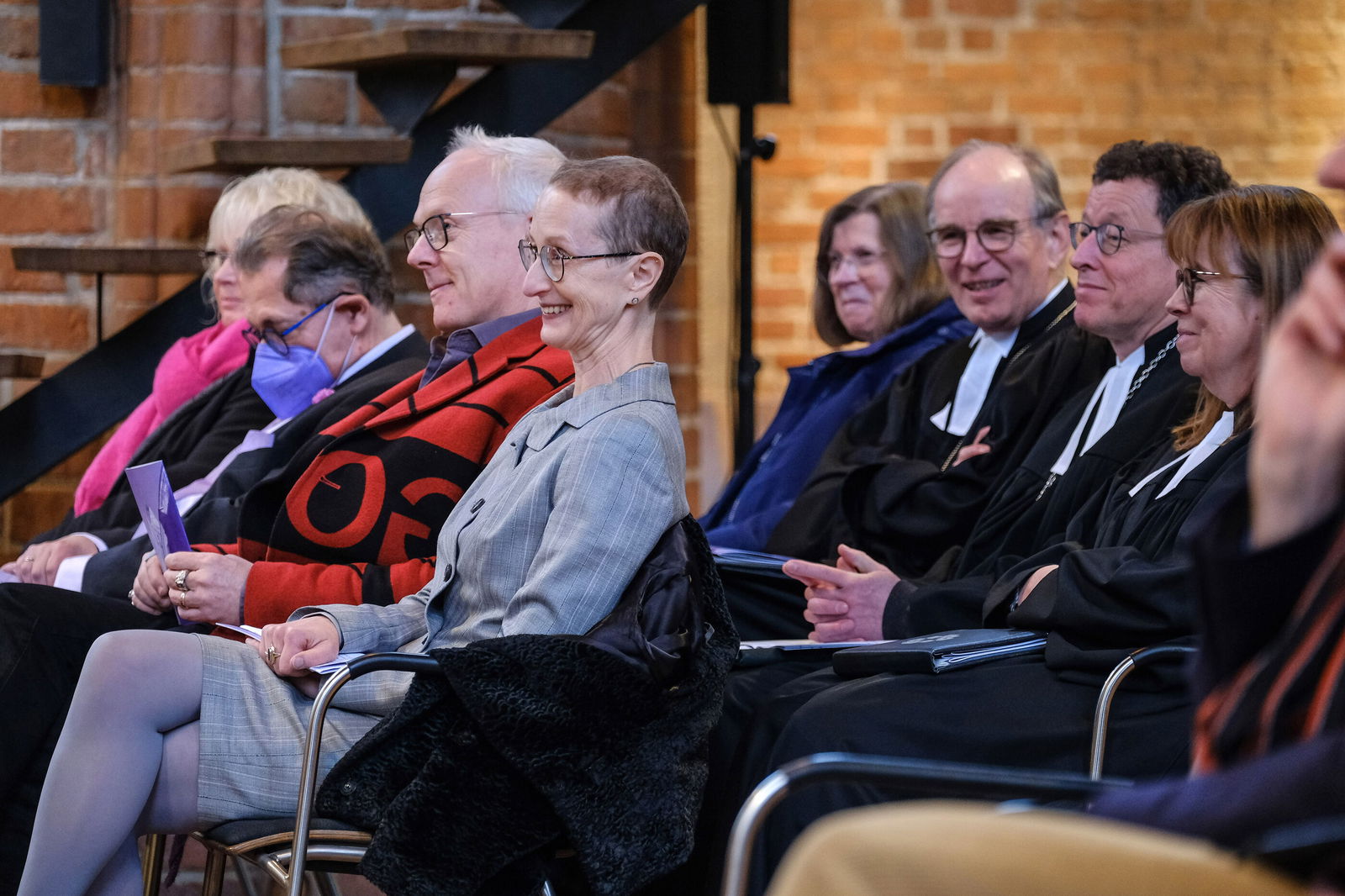 Mehrere Personen sitzen in zwei Reihen hintereinander, sie sind seitlich zu sehen.