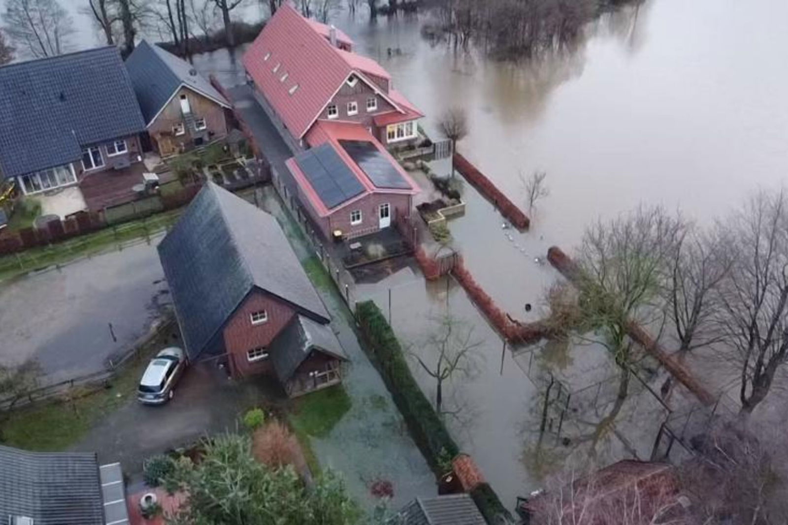 Häuser, Bäume und Hecken stehen im Wasser. 