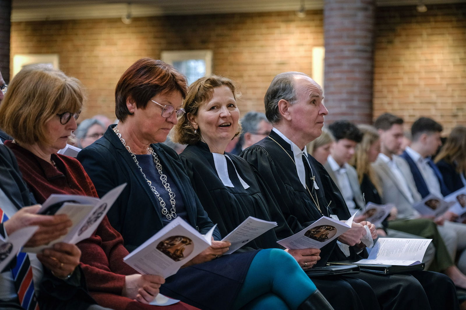 Mehreren Menschen sitzen in Reihen in einer Kirche und halten Liedzettel in Händen, die Münder im Gesang geöffnet.