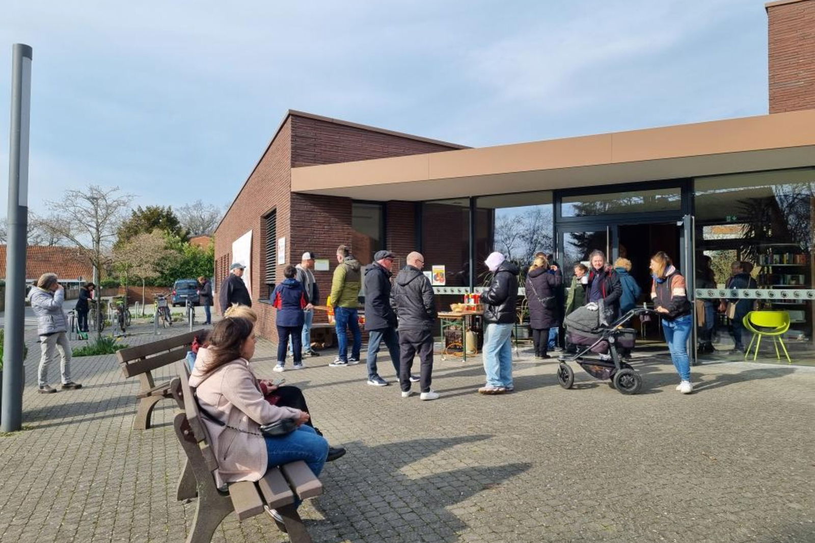 Mehrere Personen stehen vor einem Gemeindezentrum in leichtem Sonnenschein.