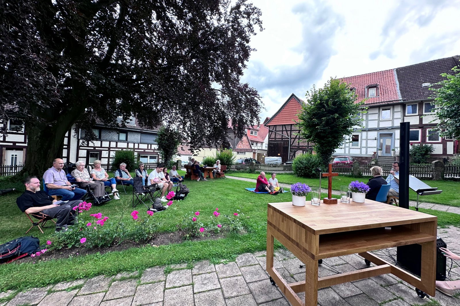 Ein hölzerner Altar auf Rollen steht vor einer Grünfläche, auf der Leute auf Stühlen sitzen. Im Hintergrund Fachwerkhäuser.