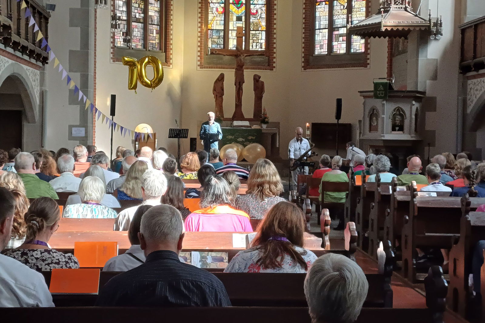 Blick in eine große Kirche, in den Bänken sieht man von hinten Leute sitzen.