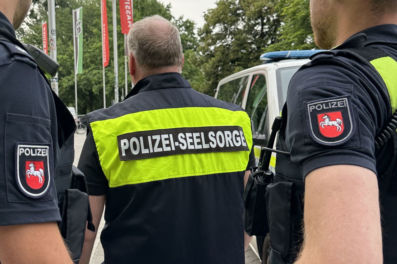 Drei männlich gelesene Personen in Polizeiuniform. Auf dem Rücken steht Polizeiseelsorge