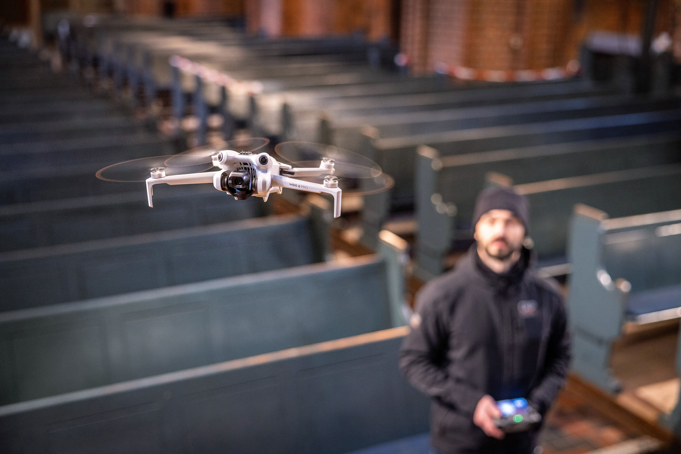Eine als Mann lesbare Person lässt eine Drohne in einer Kirche fliegen.