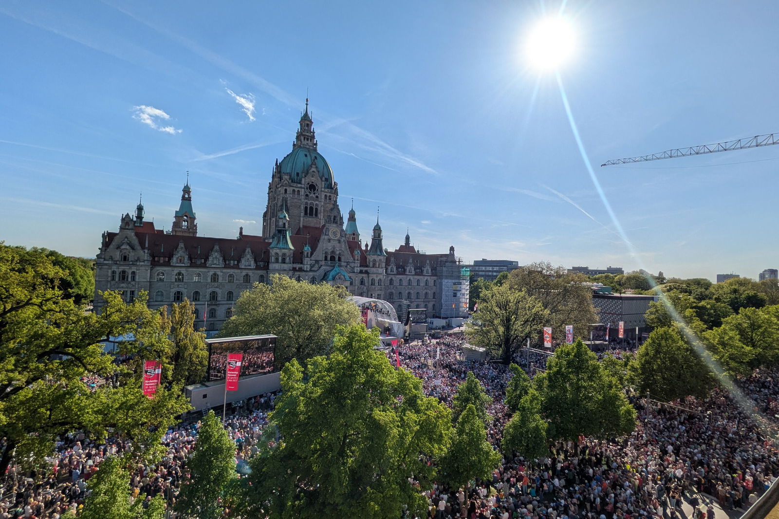Eine Luftaufnahme mit einem Rathaus, Bäumen und sehr vielen Menschen vor einer Bühne.