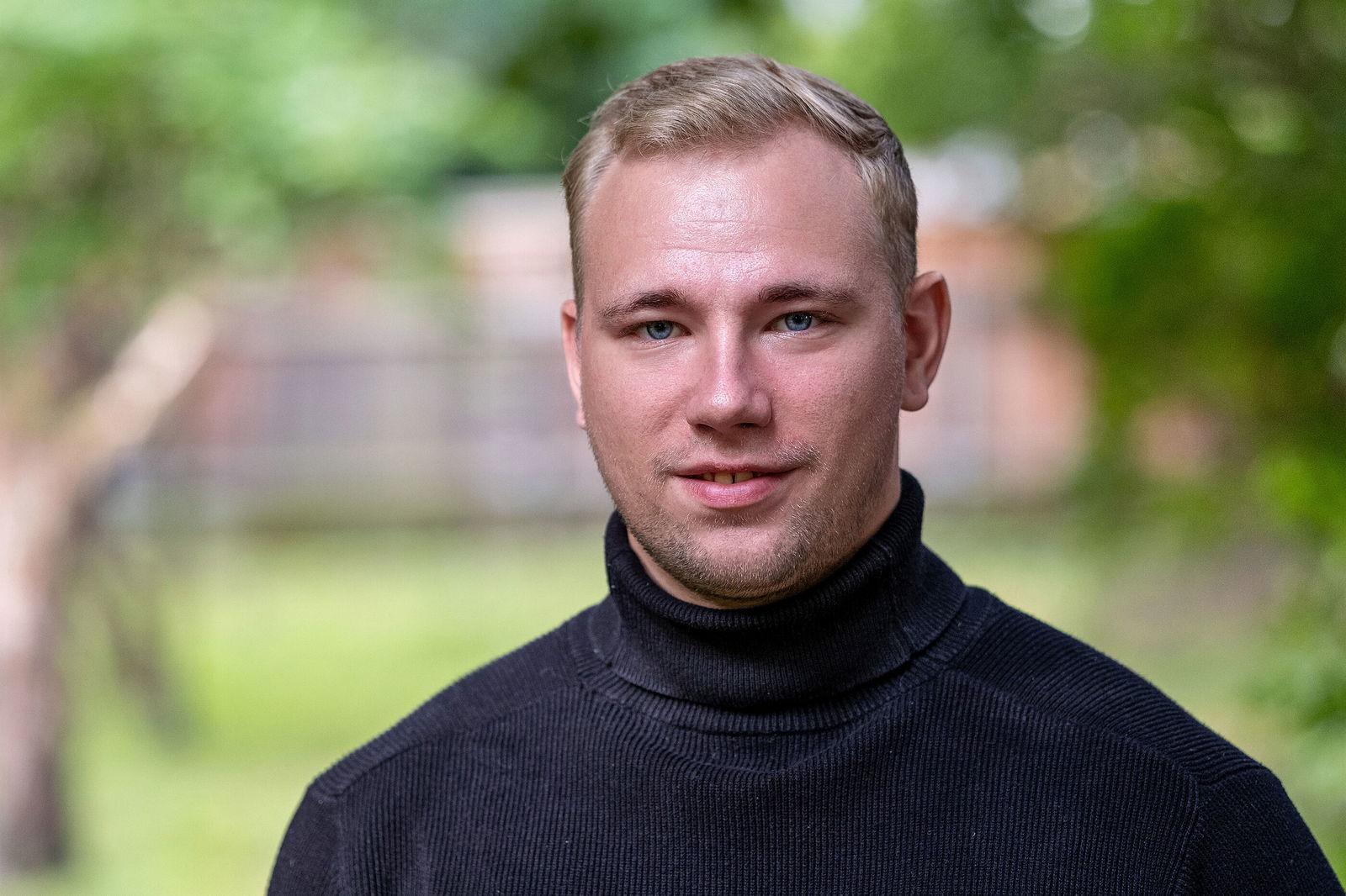 Eine junge, männlich gelesene Person mit kurzen Haaren in schwarzem Pulli.